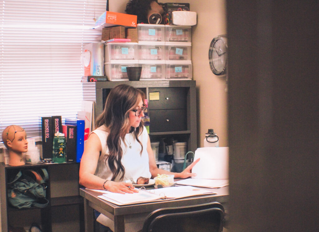 A salon owner doing payroll while eating lunch, going above and beyond other hair stylists to earn her tip.